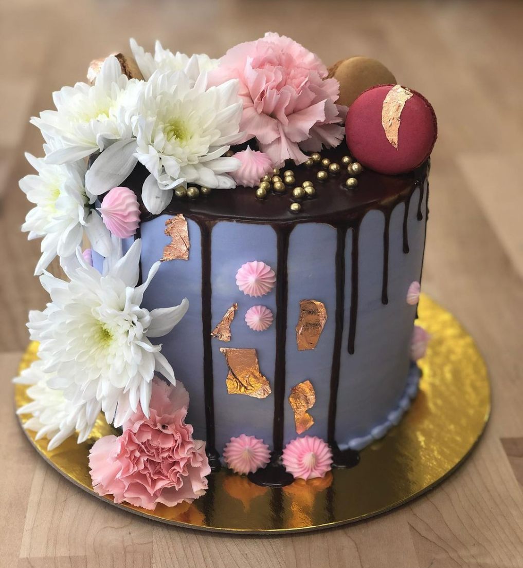 A lavender cake with a chocolate drip, fresh flowers, macarons and copper leaf