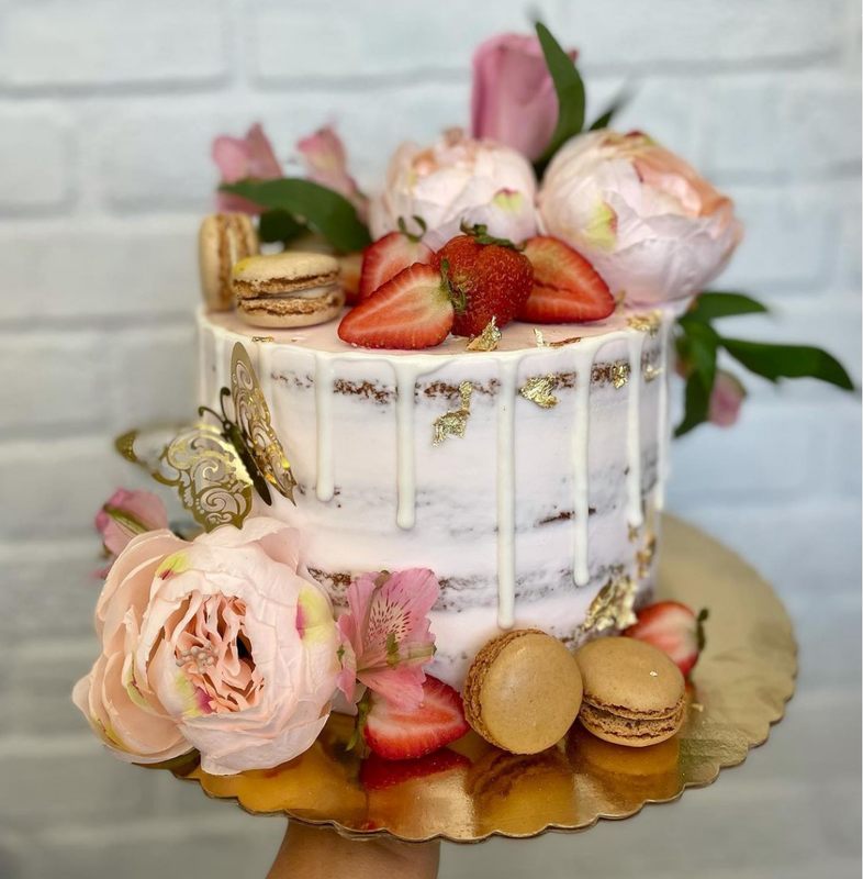 A naked cake topped with strawberries, macarons, peonies and gold leaf