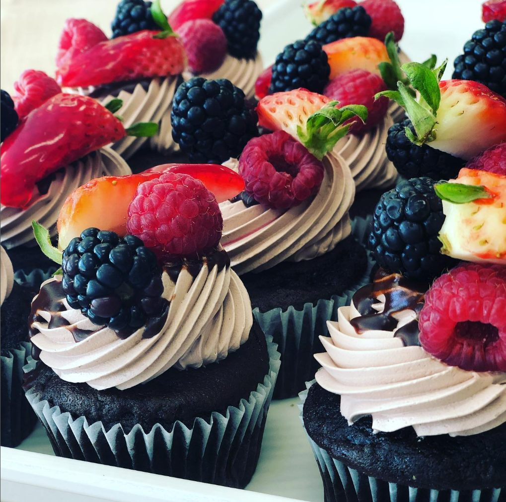 Chocolate cupcakes topped with whipped icing, strawberries, raspberries and blackberries